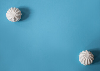 Two large white marshmallows diagonally apart on a blue background: delicious sweet background, space for text