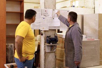 Two colleagues carpenters discussing and working with a technical blueprint drawing construction...