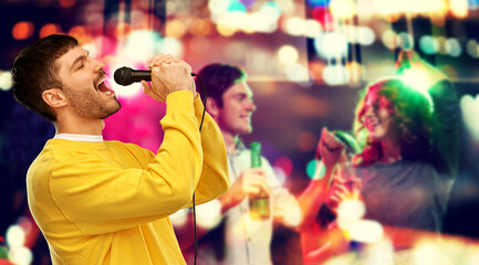 music and people concept - young man in yellow sweatshirt with microphone singing karaoke over night club background