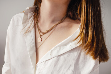 Close-up young woman in white shirt wearing golden necklaces. imalist lifestyle