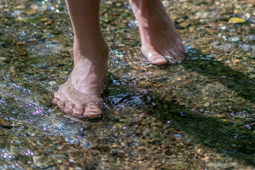 Young boy playing barefoot with clear water at a little creek using his feet and the water spring cooling his toes and legs and refreshing with the pure elixir of life in zen meditation atmosphere