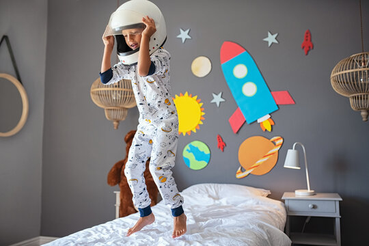 Happy little boy with astronaut helmet jumping on bed