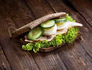 beef sandwich with dark bread, fresh green salad, eggs and cucumbers on rustic wooden table surface