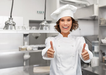 cooking, gesture and people concept - happy smiling female chef in toque showing thumbs up over restaurant kitchen background