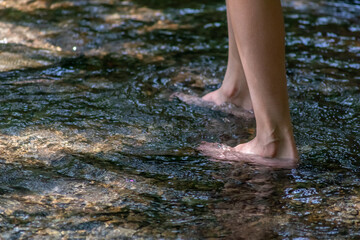 Young boy playing barefoot with clear water at a little creek using his feet and the water spring cooling his toes and legs and refreshing with the pure elixir of life in zen meditation atmosphere