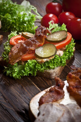 sandwich with smoked meat, green salad, fresh tomatoes and pickled cucumbers, on kitchen wooden table background