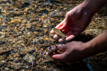 Male european hand refreshing in meditative zen atmosphere in a crystal clear water of a flat little creek with silky ripples and floating waves and sunny reflections searching for stones in the water