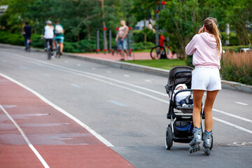 Fototapeta premium A girl rides on roller skates and pushes a pram with a small child in front of her