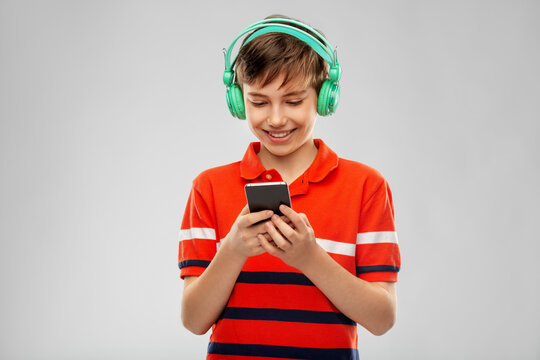 audio equipment and technology people concept - happy smiling boy in headphones listening to music on smartphone over grey background