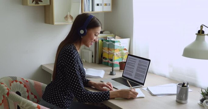 Student girl wear headphones listen audio while preparing for exams uses materials and literature on Internet make summary and text analysis. Test preparation, educational books library online concept