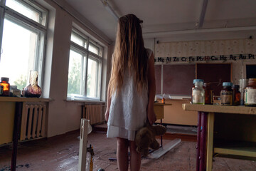 girl in a white dress with long hair and a Teddy bear in her hands stands in an abandoned chemistry room in an old ruined school. Concept of horror, mysticism