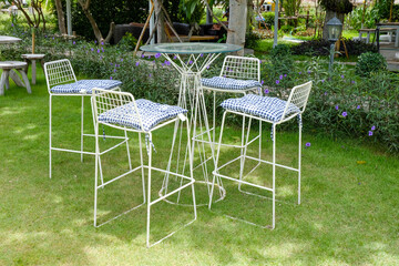 set of white metal coffee table with tall chairs with blue striped cushion in a beautiful garden,Patio furniture