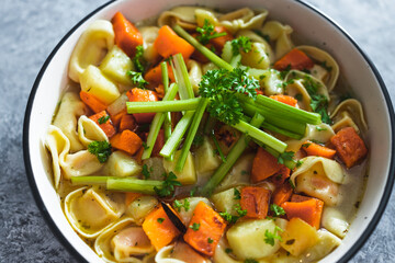 plant-based food, vegan ravioli pasta with vegetable broth topped with pumpkin and sweet potato cubes and celeri sticks
