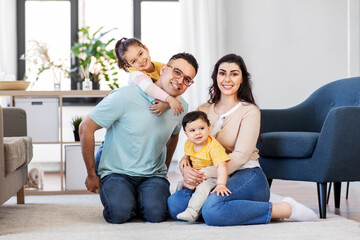 family and people concept - portrait of happy mother, father, little daughter and baby son sitting on sofa at home
