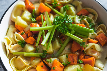 plant-based food, vegan ravioli pasta with vegetable broth topped with pumpkin and sweet potato cubes and celeri sticks