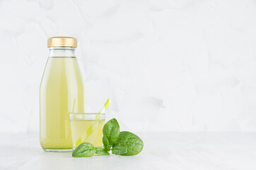 Fresh vegetable green spinach juice in glass bottle template with glass, straw, leaves on wood table and white background with copy space.