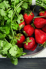 gray plate with healthy strawberries and green plants, grouped in the center on a white cloth on a dark table