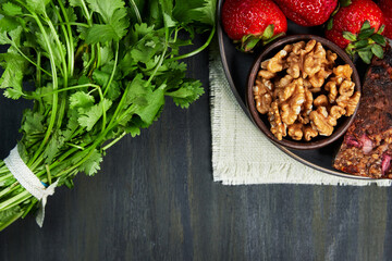 container with healthy strawberries with nuts, seed omelette and green plants, grouped on top on a white cloth on a dark table