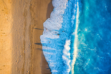Luftaufnahme eines goldenen Sandstrandes mit leuchtend,  türkisem Meer und hohen Wellen bei...
