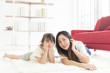 Obraz na płótnie Canvas Happiness young Asian mother and daughter lie on floor of house, smile and look at camera, family joyful together in the house