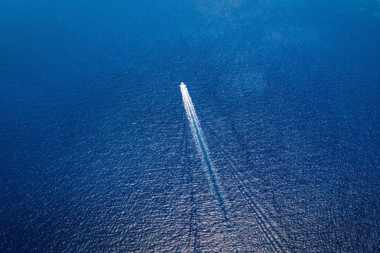 Luftaufnahme eines Motorbootes welches auf blauem, mediterranem Meer fährt und eine Spur von weißen Luftblasen und Wellen hinterlässt, mit Textfreiraum
