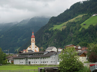Fototapeta na wymiar Summer morning foggy view on Neustift im Stubaital church at Stubaital or Stubai Valley near Innsbruck, Austria, green meadow and misty mountain peaks