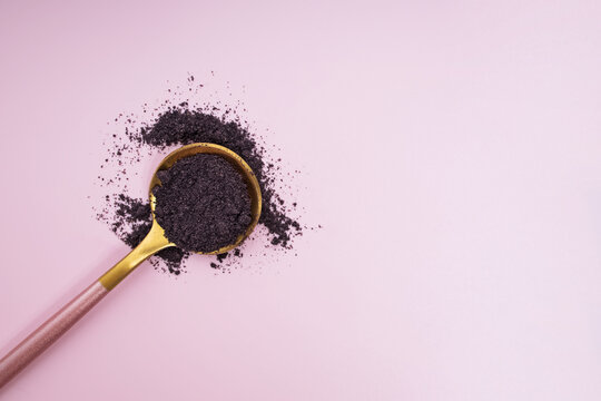 Bilberry or acai berry powder in the spoon on pink background