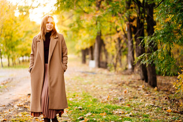 setting sun. calm woman in coat standing on footpath in autumn Park.
