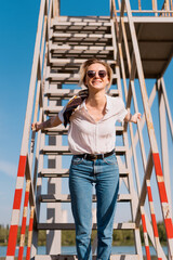 Fashion portrait of blonde girl with sunglasses wearing white shirt and blue jeans with abstract background