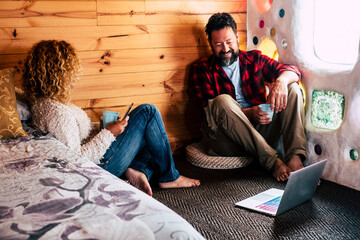Naklejka premium Adult couple inside a design room home or hotel enjoy technology computer laptop together for work in alternative lifestyle office job location - happy people together indoor