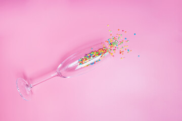 Cake confetti decorations in the champagne glass on pink background.