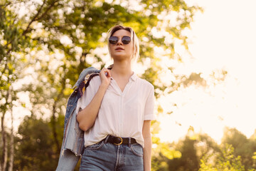 Joyful young woman in fashionable sunglasses walking in nature on a beautiful day