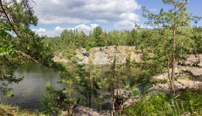 Fototapeta na wymiar Panorama of forest lake with rocky shores through the trees