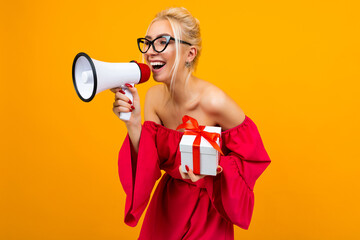 blond girl in a red dress talks about a draw with a megaphone and a gift box in hands on a yellow...