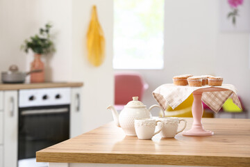 Tasty muffins with teapot and cups on table in kitchen