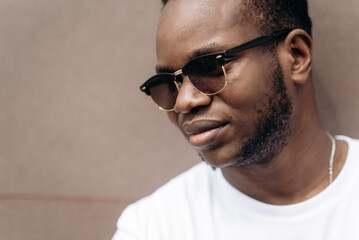 Fototapeta premium Close up man's portrait. Handsome african american guy in a white t-shirt and in sunglasses posing and smiling