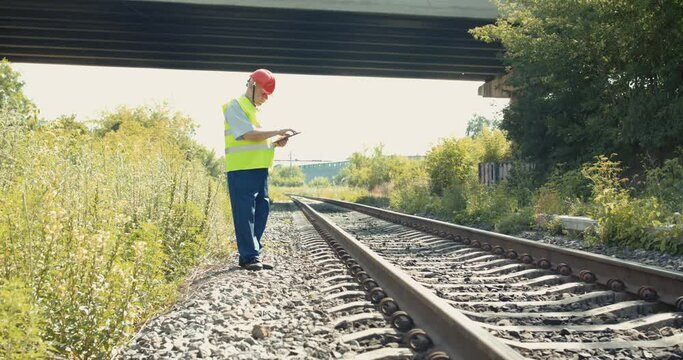 Railroader walking at the railway to check a serviceability and noting on tablet