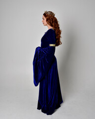 Full length portrait of  girl wearing long blue velvet gown with golden crown. standing pose with back to the camera, isolated against a studio background. © faestock