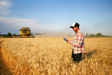 Precision farming. Farmer holding tablet for combine harvester guidance and control with modern...
