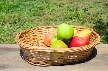 Apples and pears in a wicker basket on a rough wooden table.