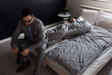 Young couple in bedroom in the morning. Woman is in the bed, and man is going to work. When Work Interferes with Love.