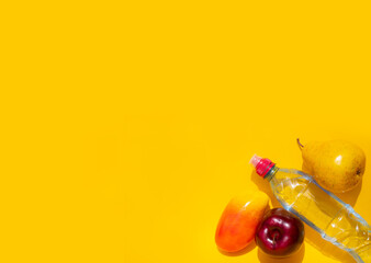 Fresh and healthy fruits: red Apple, yellow pear and mango lie on a yellow background next to a sports water bottle. Concept of proper nutrition, place for text, top view