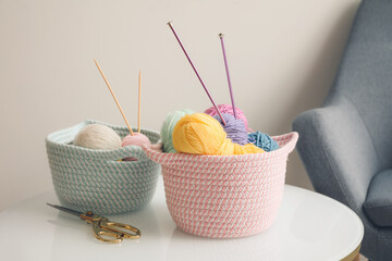 Wicker baskets with knitting yarn on table in room