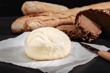 Loaf of bread with butter and knife. Dark background, side view