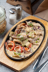 Vegetables baked and served in cast iron skillet with cream and onions, top view and close up, with pepper and salt shakers on background