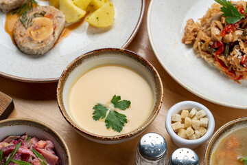 A bowl of cream soup among other meals on wooden table, close up