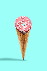 Sweet donut glazed by pink icing sprinkled with marshmallow in wafer cone on turquoise background. Treats, unhealthy nutrition. Close up, copy space