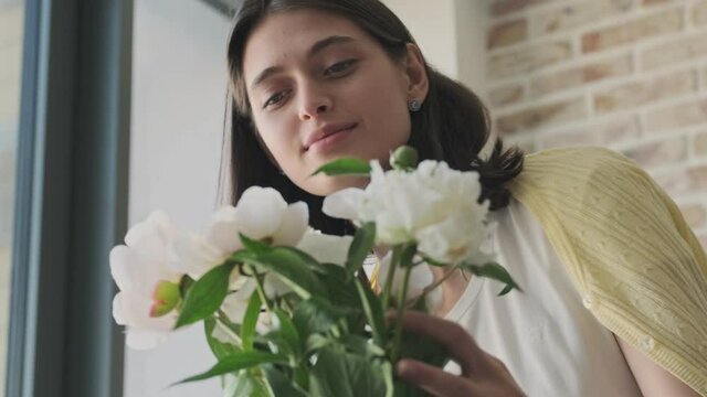 Young pleased optimistic cute woman indoors at home with beautiful flowers