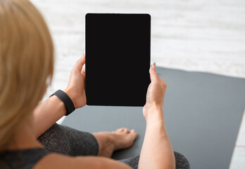 Home workout with devices. Adult woman with fitness tracker and tablet sits on mat