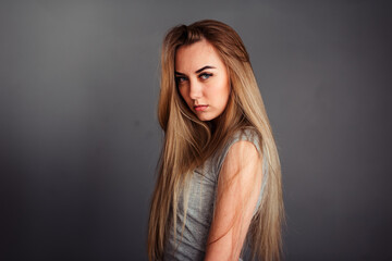Naklejka premium A girl with blue eyes looks piercingly into the frame, wrapping her hair in a gray background